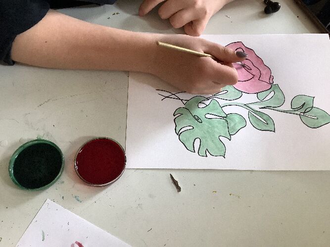 Eine Schülerin malt mit Pflanzenfarbe eine Blume